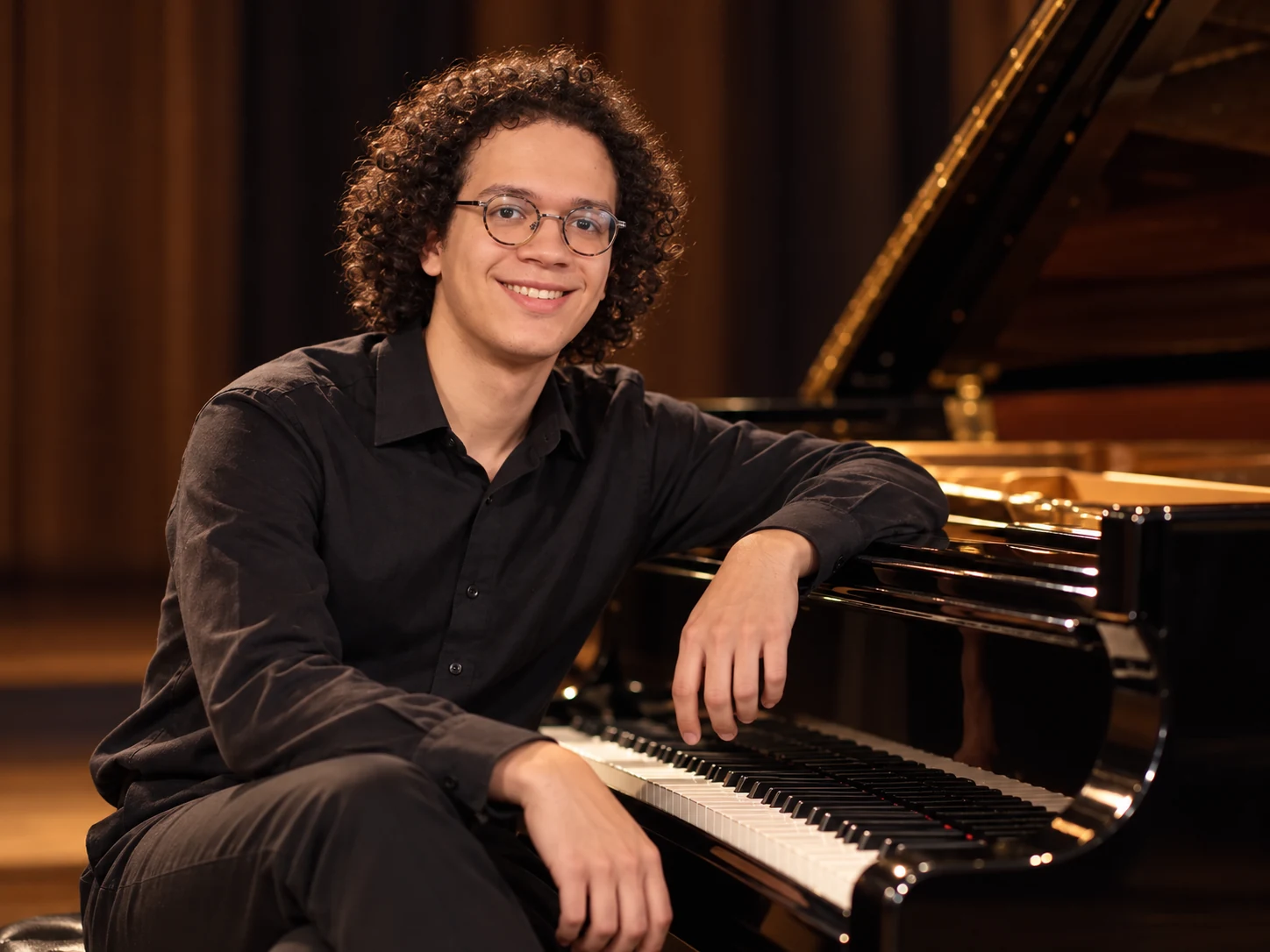 Lou Hägi seated casually at a glossy black concert grand piano
